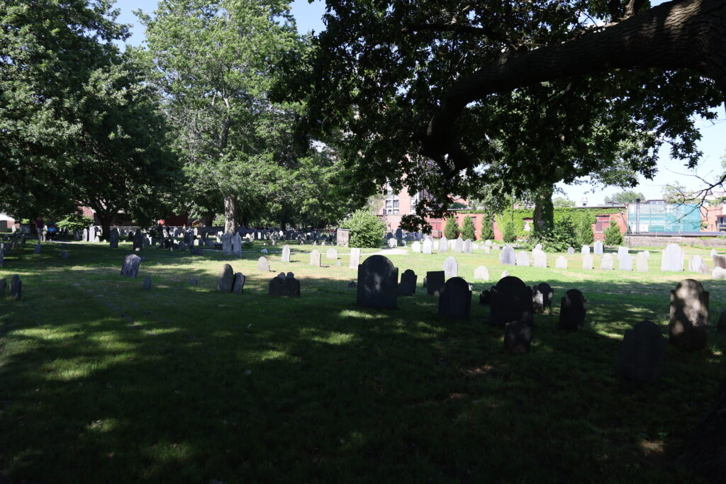 Rows of old slate headstones under shade trees in the Old Burying Point, Salem