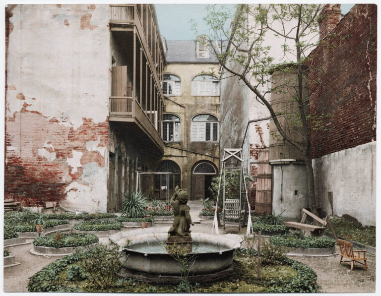 A tinted photo of a walled courtyard with a fountain, peeling plaster and wooden galleries
