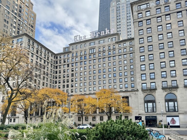 The Drake Hotel's limestone towers and rooftop sign above autumn trees