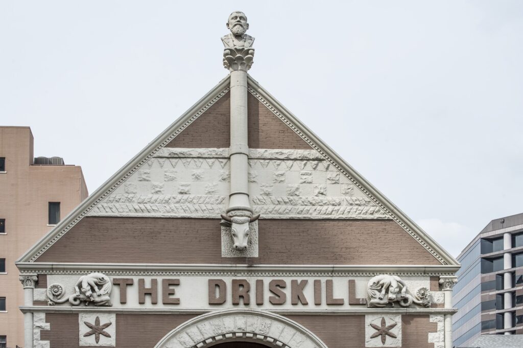 A stone gable of the Driskill hotel with THE DRISKILL in raised letters and a carved bust at its peak