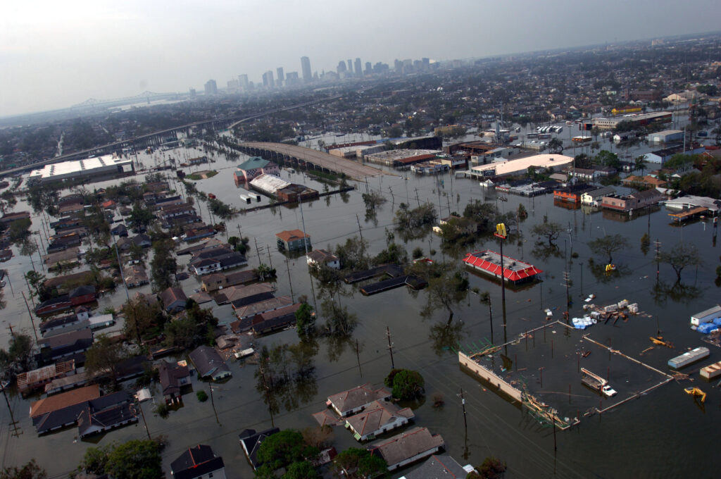 An aerial view of rooftops and streets standing in floodwater, with downtown towers in the distance