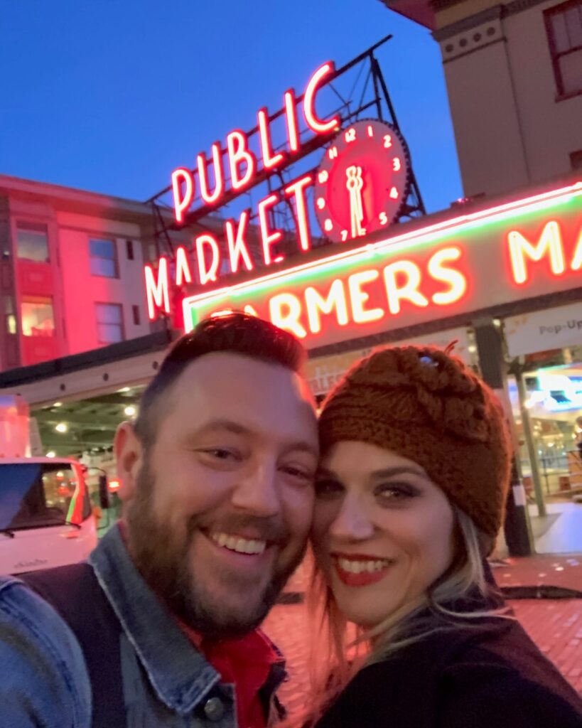 Harry and Leigh Anne Kautzman under the Public Market sign at Pike Place Market at night.