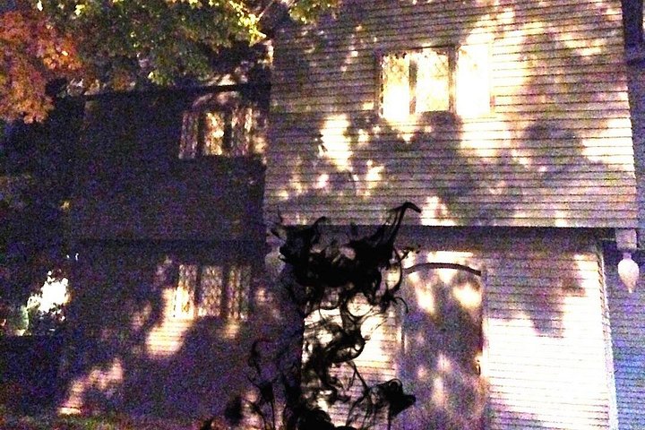 A strange black mass passes by the front door of the Witch House while something watches from the upper left window