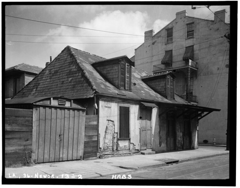 A small, weathered cottage with a steep hipped roof and dormers, its plaster worn back to the brick in places