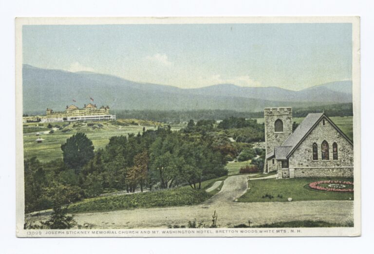 A small stone church with a square tower in the foreground, and the long hotel with red-flagged towers across a green valley