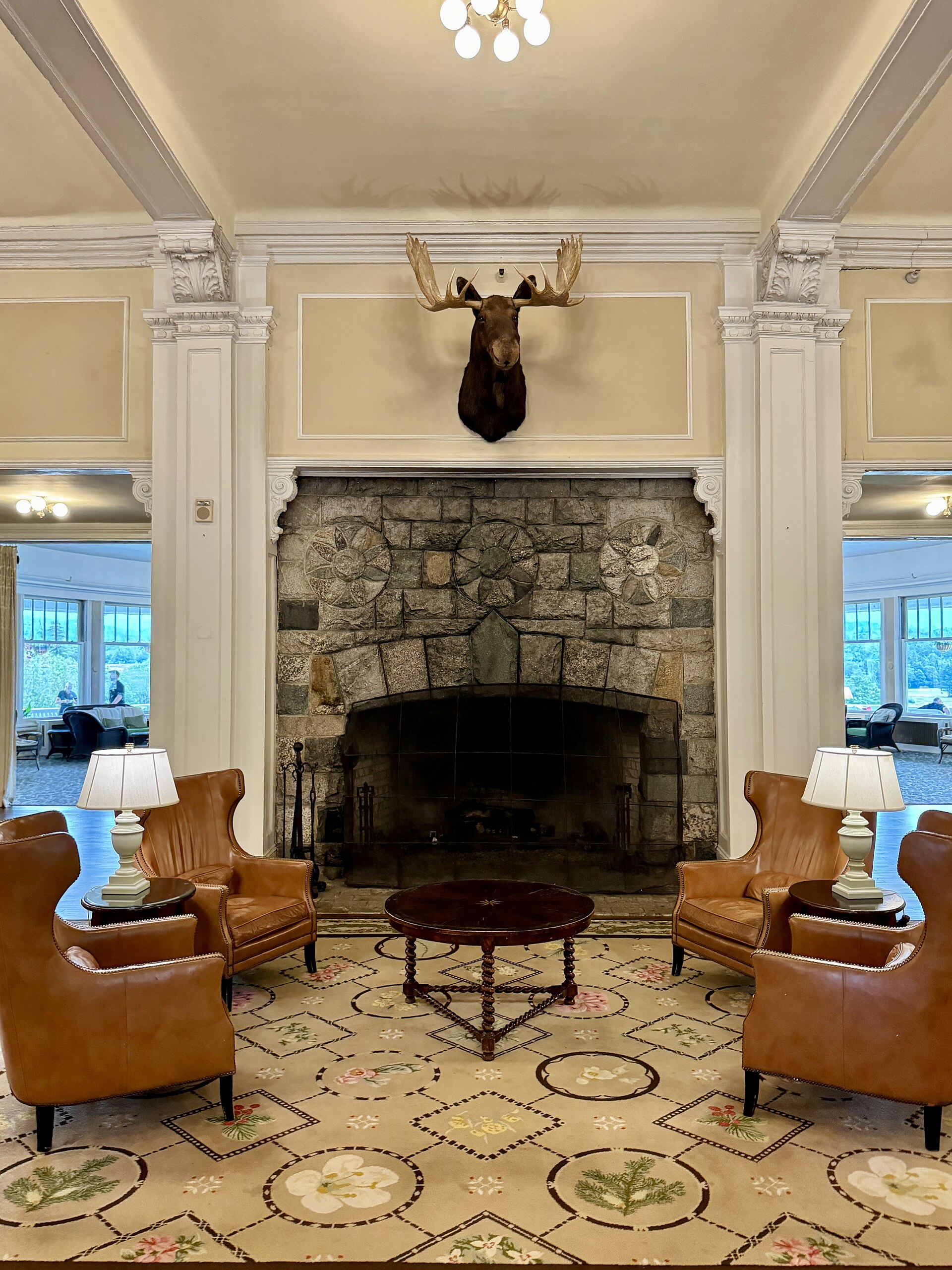 A large granite fireplace under a moose head, with leather armchairs on either side