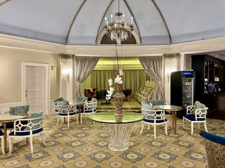 A round lounge under a ribbed, pale blue dome and a chandelier, with curtains drawn back from an alcove at the far end