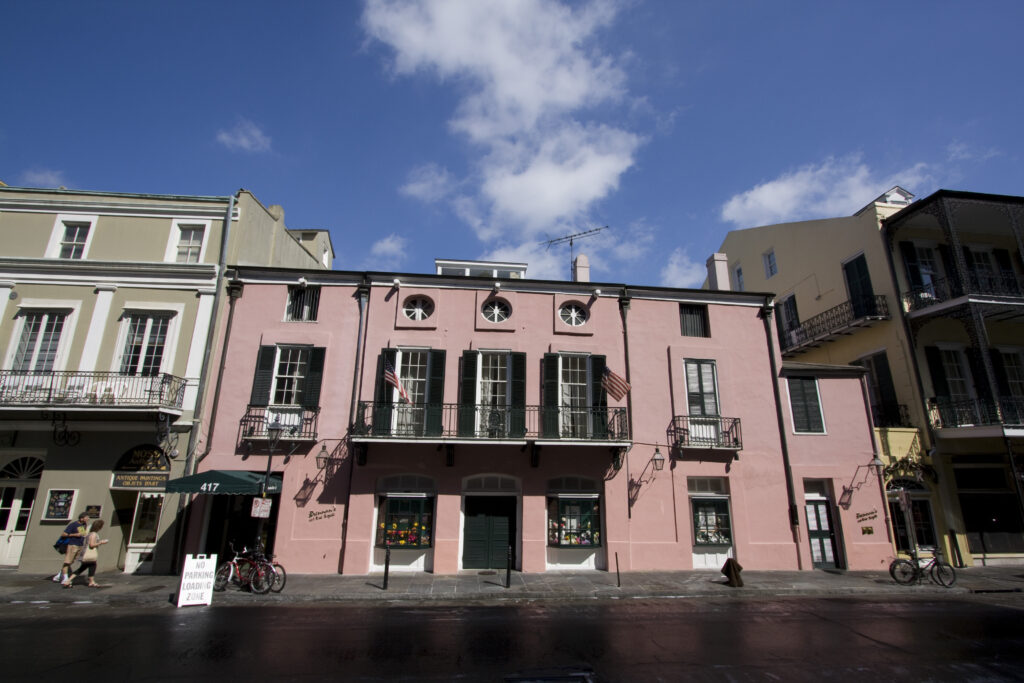 A pink two-story building with black shutters and iron balconies on a sunny Royal Street