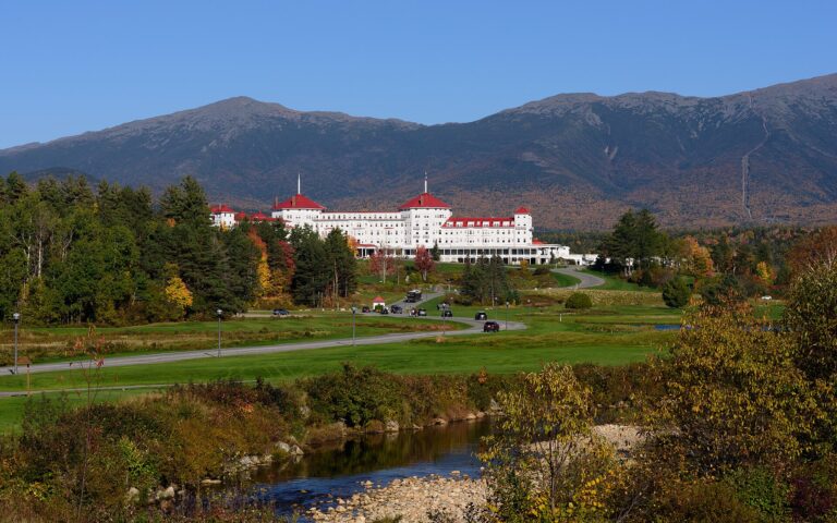 The long white hotel with red roofs in autumn, with forested mountains behind it
