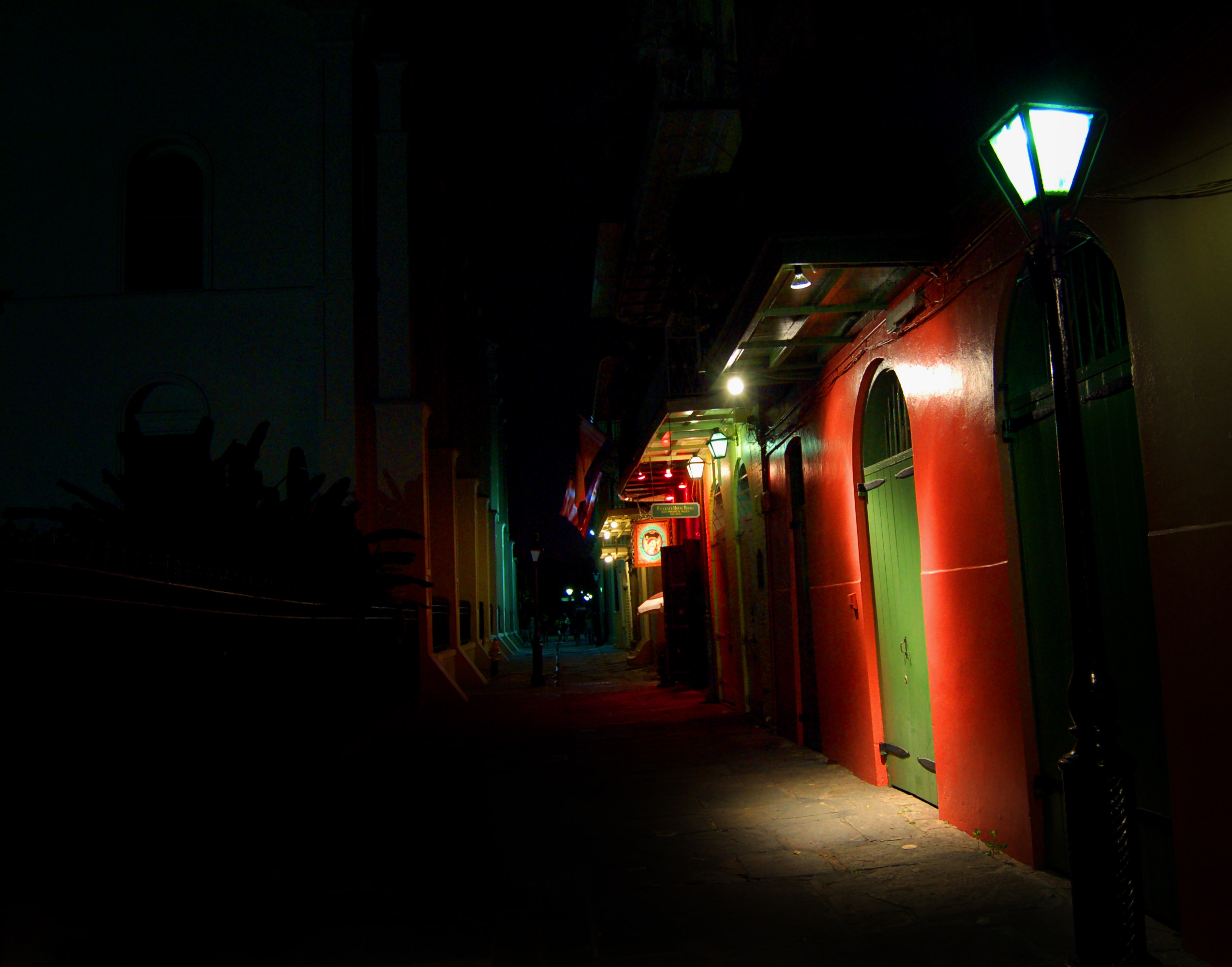 A narrow flagstone alley at night, lit by a lantern and a red-painted doorway