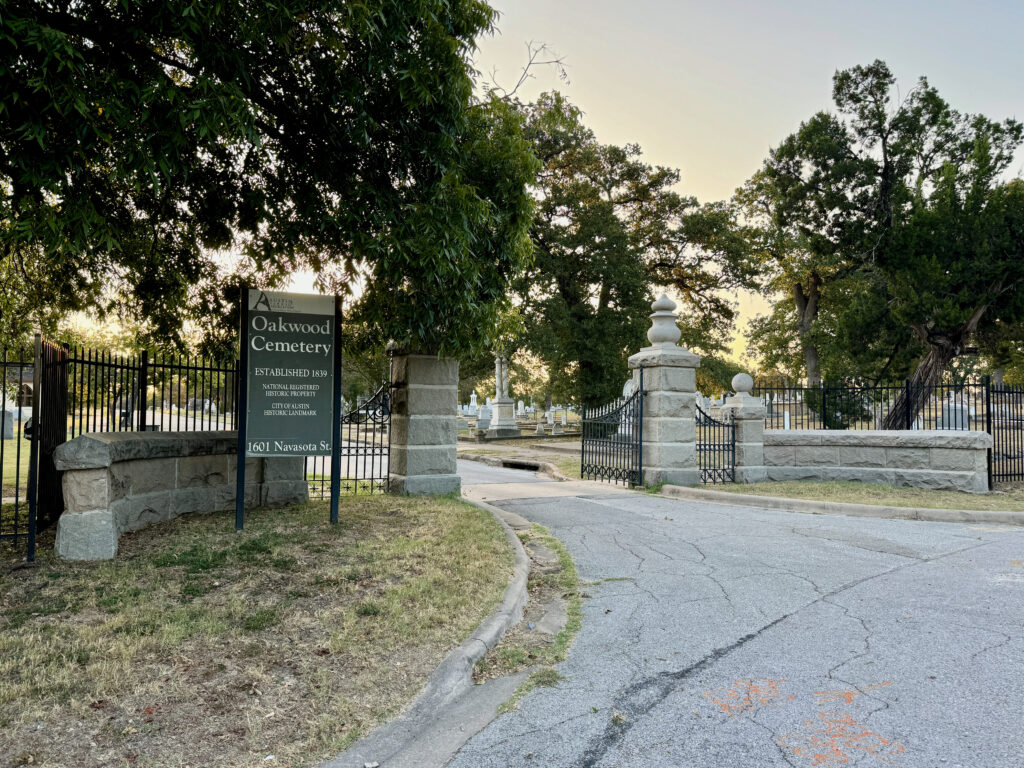 Stone gateposts and an iron fence at the entrance to Oakwood Cemetery, with a sign reading Established 1839
