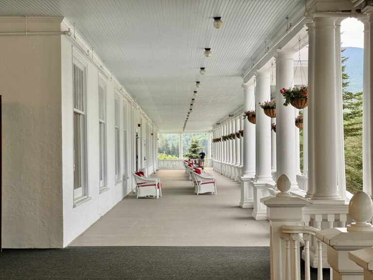 A long covered veranda with white columns, hanging flower baskets and rocking chairs