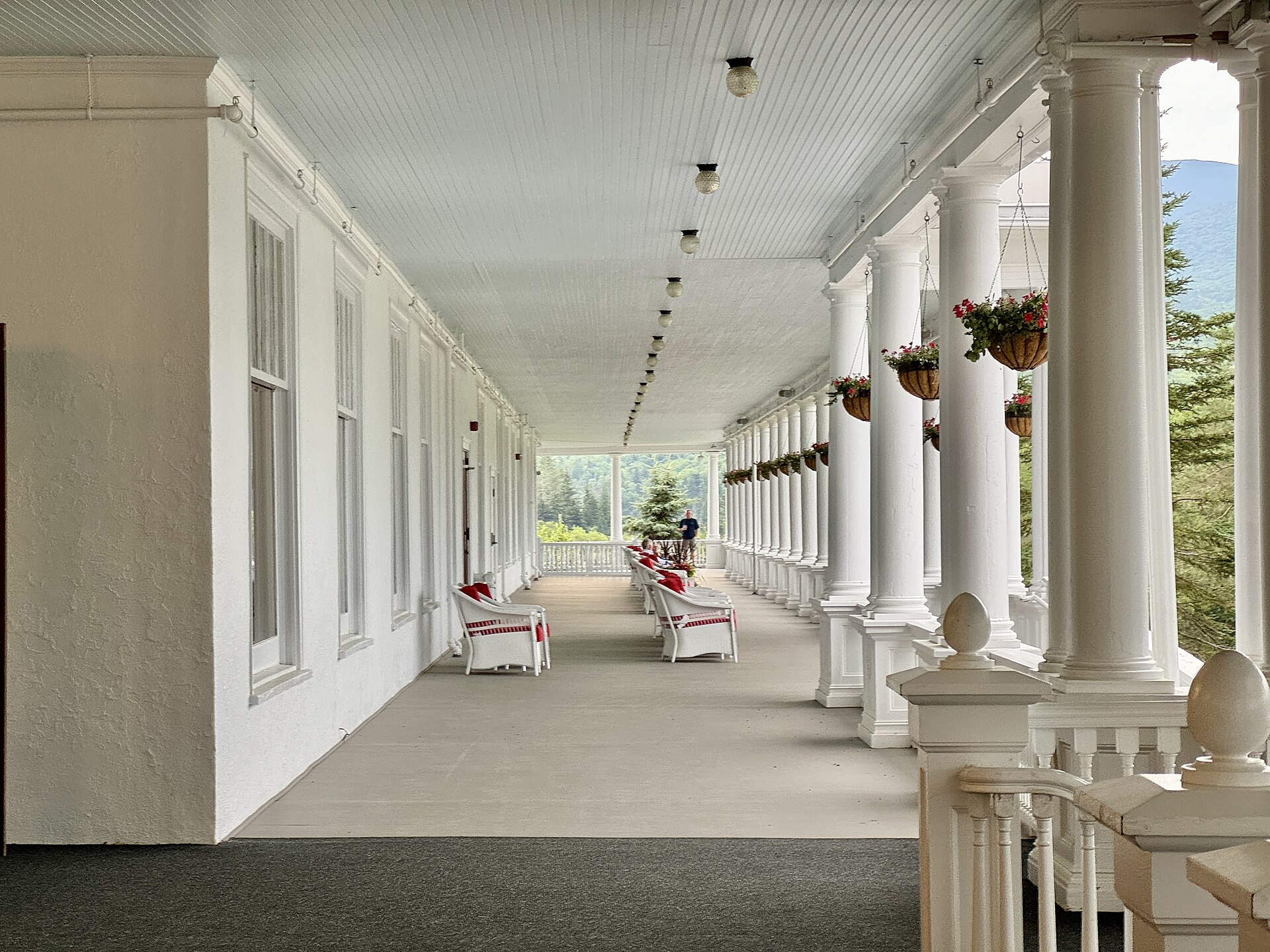 A long covered veranda with white columns, hanging flower baskets and rocking chairs