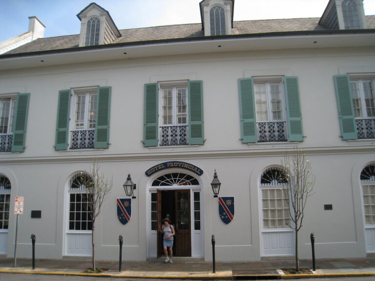 A white two-story building with green shutters, arched ground-floor windows and dormers in the roof