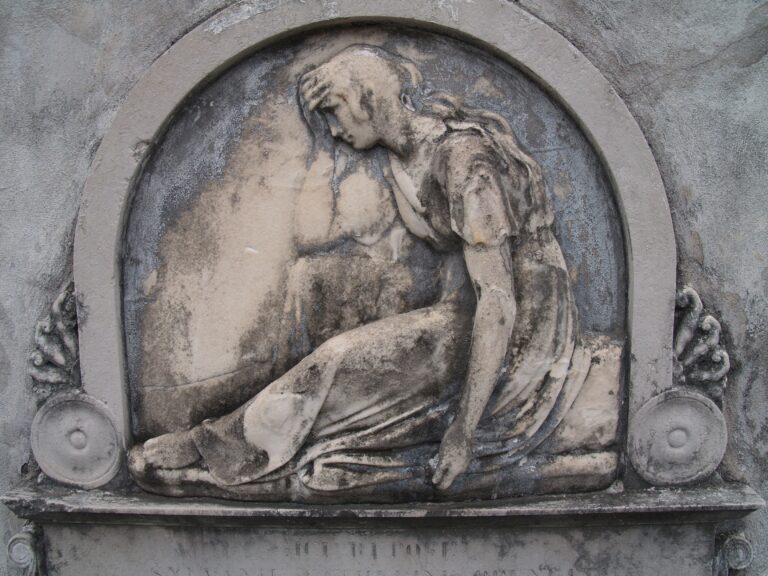 A stone relief of a seated woman bowing her head into her hand, inside an arch