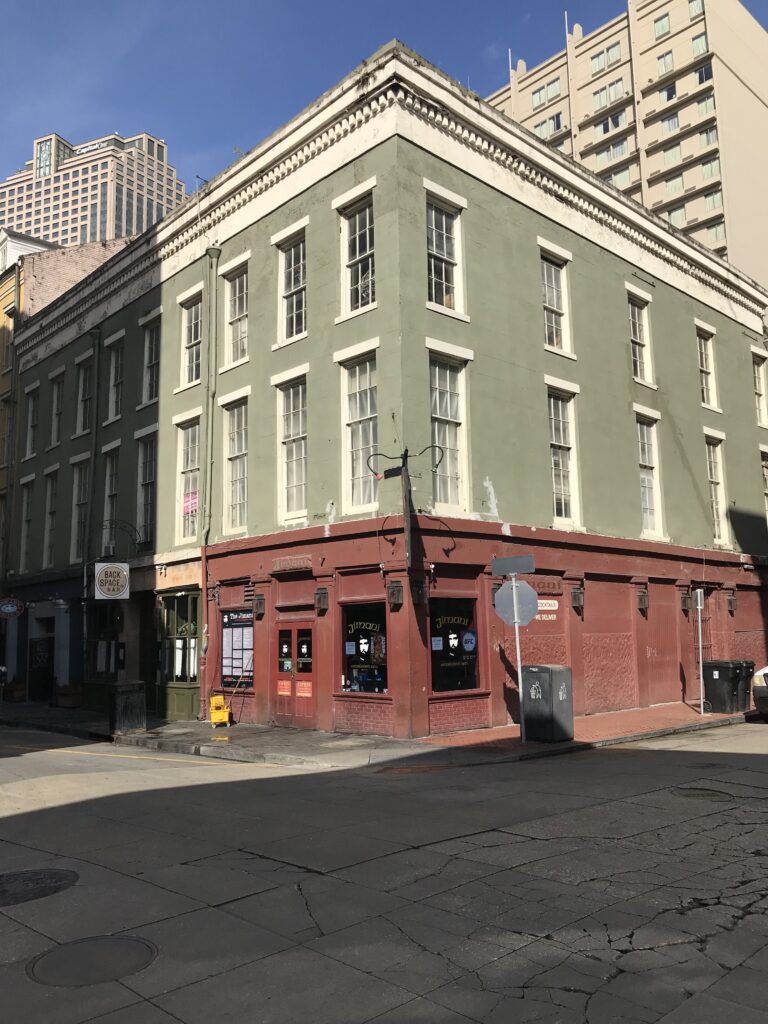 A three-story corner building painted green above a dark red ground floor, under a clear sky