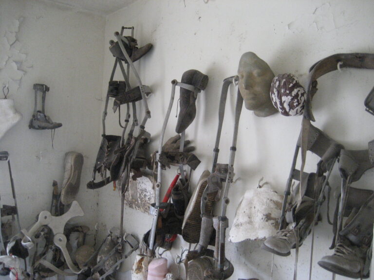 Old crutches, leg braces, shoes and a plaster face hanging on a peeling white wall