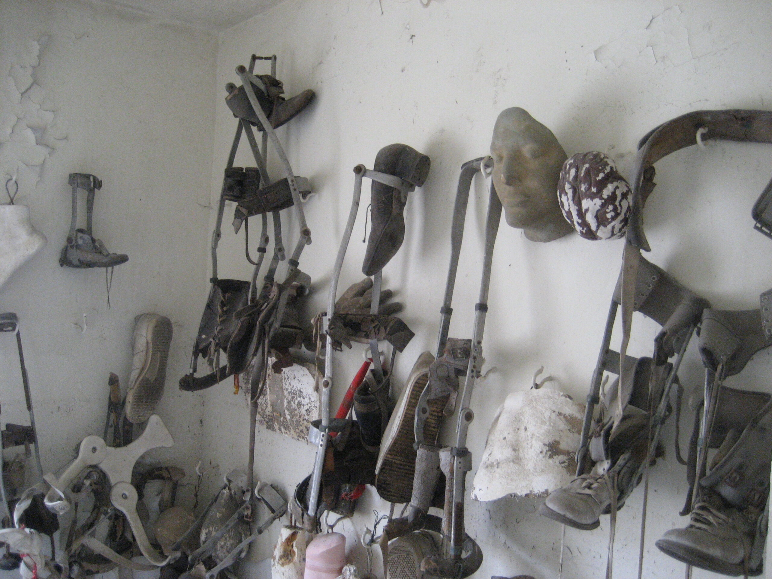 Old crutches, leg braces, shoes and a plaster face hanging on a peeling white wall