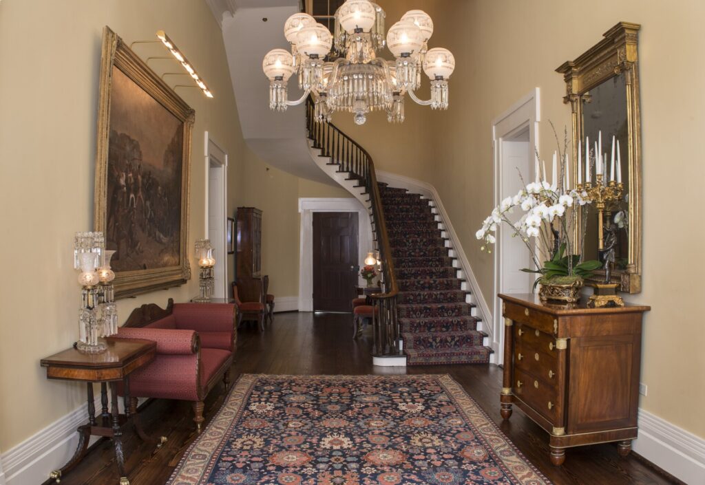 The entry hall of the Texas Governor's Mansion: a curving staircase, a chandelier, a red sofa, and a patterned rug