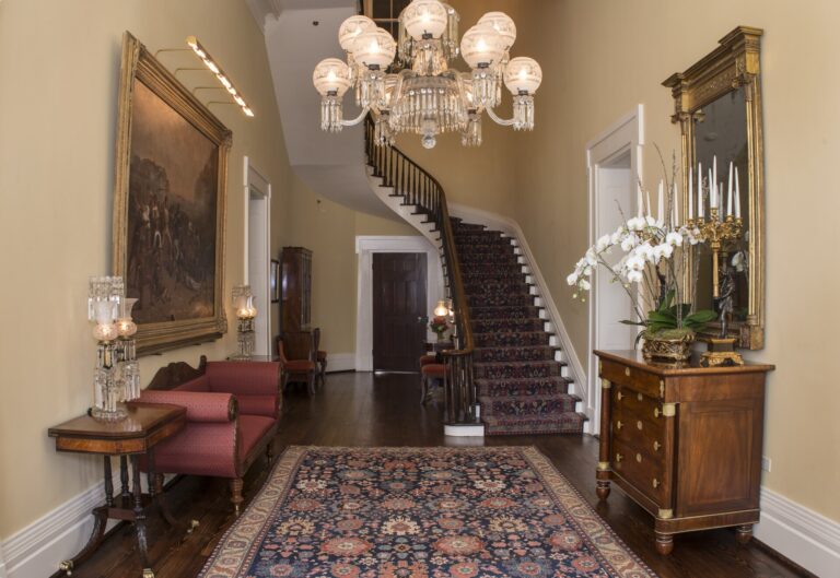 The entry hall of the Texas Governor's Mansion: a curving staircase, a chandelier, a red sofa, and a patterned rug