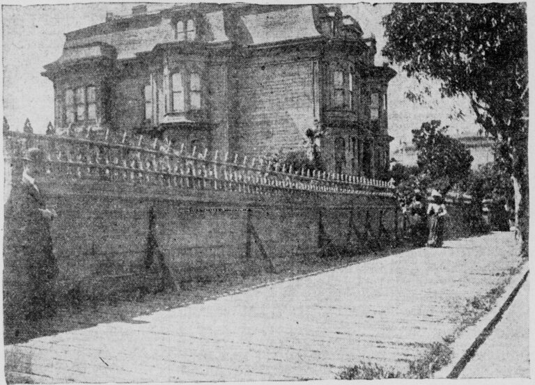 A grainy newspaper photograph of a three-storey Victorian mansion with a mansard roof, set back behind a long, high garden wall with an iron railing along a sloping sidewalk