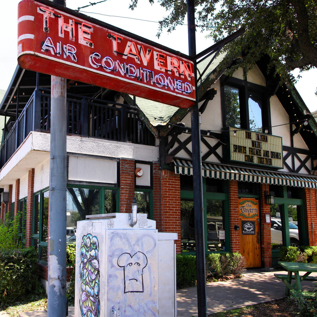 A half-timbered pub behind a red neon sign reading The Tavern, Air Conditioned