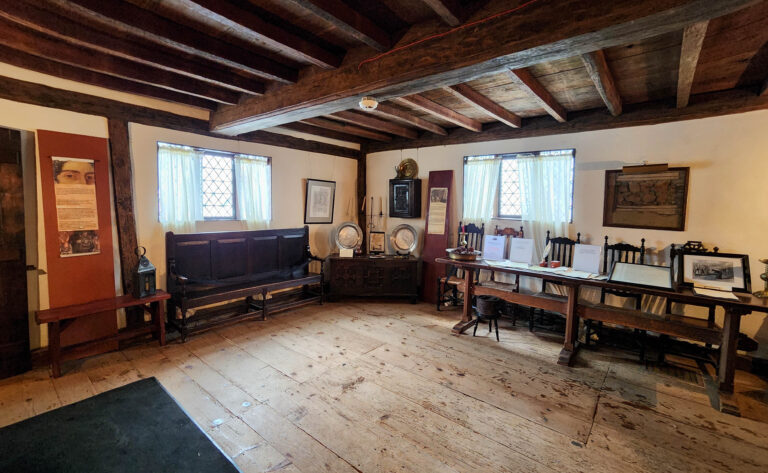 A wide brick hearth hung with iron pots and cooking tools inside the Witch House