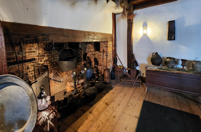 A long table set with period dishes under the exposed ceiling beams of the Witch House's hall
