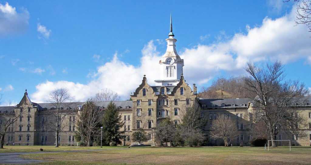 The long sandstone main building of the former Weston State Hospital, with its white central clock tower, seen across a wide lawn
